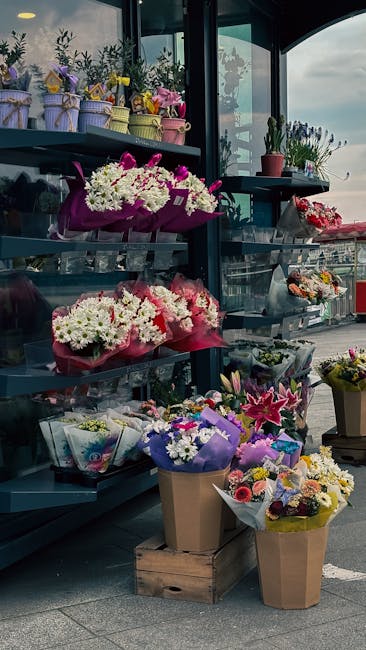 A young delivery person wearing a bright yellow vest and a red cap is holding a bouquet of fresh white hydrangeas wrapped in white paper. They are reaching out to carefully place the floral gift on a 